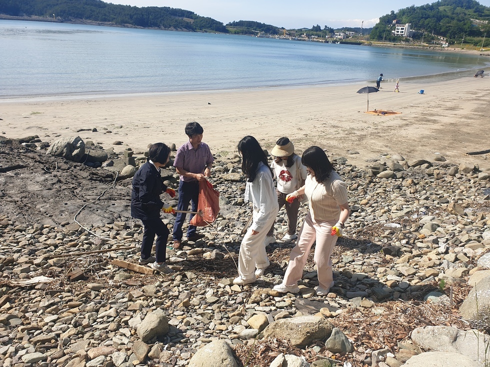 해변가에서 쓰레기를 줍는 5명의 사람들