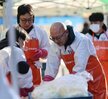 ‘따뜻한 가치, 섬세한 서비스, 든든한 도시관리공단 여수시도시관리공단 노·사 합동 동행 봉사단’이라는 문구가 적힌 현수막을 들고 여수시도시관리공단 임직원들이 김장 나눔 봉사활동을 기념하며 단체 사진을 촬영한 모습이다. 다양한 연령대의 임직원 20여 명이 모였으며, 일부는 오렌지색 앞치마와 마스크를 착용한 상태로, 김장박스가 가득 실린 트럭과 텐트 옆에서 밝은 표정으로 포즈를 취하고 있다. 