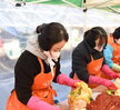 ‘따뜻한 가치, 섬세한 서비스, 든든한 도시관리공단 여수시도시관리공단 노·사 합동 동행 봉사단’이라는 문구가 적힌 현수막을 들고 여수시도시관리공단 임직원들이 김장 나눔 봉사활동을 기념하며 단체 사진을 촬영한 모습이다. 다양한 연령대의 임직원 20여 명이 모였으며, 일부는 오렌지색 앞치마와 마스크를 착용한 상태로, 김장박스가 가득 실린 트럭과 텐트 옆에서 밝은 표정으로 포즈를 취하고 있다. 
