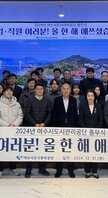 '2024년 여수시도시관리공단 종무식 임·직원 여러분! 올 한 해 애쓰셨습니다. 여수시도시관리공단 일자 : 2024.21.31 (화)'라는 문구가 적힌 대형 화면을 배경으로 같은 문구가 적혀진 현수막을 들고 여수시도시관리공단 임직원들이 단체로 촬영한 기념사진이다. 사진에는 30여 명의 임직원이 참여했으며 연령대는 20대에서 60대까지 다양하다. 2명의 남자 직원의 현수막을 길에 펼치며 앉아 있고, 가운데에는 50대 남성과 여성이 나란히 서 있으며, 전체적으로 단정한 복장으로 정돈된 분위기 속에서 한 해의 마무리를 기념하고 있다.