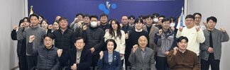 '따뜻한 가치, 섬세한 서비스, 든든한 도시관리공단 2025년 여수시도시관리공단 시무식 여수도시관리공단 일자 : 2025.1.2(목)'이라는 문구가 적힌 현수막을 배경으로, 여수시도시관리공단 임직원들이 시무식을 기념하여 단체 촬영한 사진이다. 총 30여 명의 임직원이 참여했으며 연령대는 20대부터 60대까지 다양하다. 앞줄에는 4명이 의자에 앉아 있고, 오른쪽에는 휠체어를 탄 인물이 위치해 있다. 그 뒤편으로는 여러 명의 임직원들이 힘찬 주먹 인사를 하며 포즈를 취하고 있다.