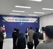 '따뜻한 가치, 섬세한 서비스, 든든한 도시관리공단 2025년 여수시도시관리공단 시무식 여수도시관리공단 일자 : 2025.1.2(목)'이라는 문구가 적힌 현수막을 배경으로, 여수시도시관리공단 임직원들이 시무식을 기념하여 단체 촬영한 사진이다. 총 30여 명의 임직원이 참여했으며 연령대는 20대부터 60대까지 다양하다. 앞줄에는 4명이 의자에 앉아 있고, 오른쪽에는 휠체어를 탄 인물이 위치해 있다. 그 뒤편으로는 여러 명의 임직원들이 힘찬 주먹 인사를 하며 포즈를 취하고 있다.
