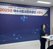 '따뜻한 가치, 섬세한 서비스, 든든한 도시관리공단 2025년 여수시도시관리공단 시무식 여수도시관리공단 일자 : 2025.1.2(목)'이라는 문구가 적힌 현수막을 배경으로, 여수시도시관리공단 임직원들이 시무식을 기념하여 단체 촬영한 사진이다. 총 30여 명의 임직원이 참여했으며 연령대는 20대부터 60대까지 다양하다. 앞줄에는 4명이 의자에 앉아 있고, 오른쪽에는 휠체어를 탄 인물이 위치해 있다. 그 뒤편으로는 여러 명의 임직원들이 힘찬 주먹 인사를 하며 포즈를 취하고 있다.