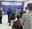 '따뜻한 가치, 섬세한 서비스, 든든한 도시관리공단 2025년 여수시도시관리공단 시무식 여수도시관리공단 일자 : 2025.1.2(목)'이라는 문구가 적힌 현수막을 배경으로, 여수시도시관리공단 임직원들이 시무식을 기념하여 단체 촬영한 사진이다. 총 30여 명의 임직원이 참여했으며 연령대는 20대부터 60대까지 다양하다. 앞줄에는 4명이 의자에 앉아 있고, 오른쪽에는 휠체어를 탄 인물이 위치해 있다. 그 뒤편으로는 여러 명의 임직원들이 힘찬 주먹 인사를 하며 포즈를 취하고 있다.