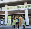 '따뜻한 가치, 섬세한 서비스, 든든한 도시관리공단 여수시도시관리공단 노‧사 합동 동행 봉사단' 이라는 문구가 적힌 대형 현수막을 펼쳐 들고, 그 뒤로는 '아름다운 나눔보따리 희망을 배달합니다.' 등의 문구가 적힌 현수막이 붙은 여수시청 앞 계단에서 기념촬영한 모습이다. 여수 시청 건물에는 여수시 남해안 거점도시 미항 여수라는 현수막이 걸려있다. 생필품이 담긴 나눔 보따리를 전달하기 위해 모인 여수시도시관리공단 봉사단 50여 명이 단체로 서 있으며, 대체로 20대에서 50대 연령대의 직원들로 구성되어 있다. 일부는 손가락 하트나 엄지손가락을 들어 보이며 포즈를 취하고 있다.