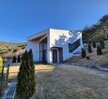 봉황산자연휴양림 신축동의 욕실 내부 모습으로, 세면대와 샤워실이 분리된 구조로 깔끔하게 구성되어 있다. 전반적으로 회색 타일을 사용하여 차분하고 모던한 분위기를 자아내며, 세면대는 넓은 상판 위에 원형 라인의 세련된 화이트 세면볼이 놓여 있고, 그 위로는 아치형 거울이 설치되어 있다. 우측으로는 투명 유리 칸막이로 분리된 샤워 공간이 있으며, 안쪽에는 변기와 샤워기가 설치되어 있다. 욕실 입구 바닥에는 파란 슬리퍼가 가지런히 놓여 있어 실용적인 면도 더해준다.