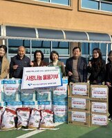 '따뜻한 가치, 섬세한 서비스, 든든한 도시관리공단 사랑나눔 물품기부 여수시도시관리공단 임직원 일동' 이라는 문구가 적힌 팻말을 들고 있고, '사랑나눔 물품기부' 라는 스티커가 붙은 쌀, 화장지, 생필품 박스 등이 정돈된 상태로 쌓여 있다. 해당 물품들을 기부한 여수시도시관리공단 임직원 7명(30대에서 50대 연령대)이 건물 외부 공간에서 손가락 하트 포즈를 취하며 기념촬영한 단체 사진이다.