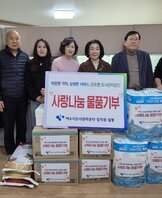 '따뜻한 가치, 섬세한 서비스, 든든한 도시관리공단 사랑나눔 물품기부 여수시도시관리공단 임직원 일동' 이라는 문구가 적힌 팻말을 들고 있고, '사랑나눔 물품기부' 라는 스티커가 붙은 쌀, 화장지, 생필품 박스 등이 정돈된 상태로 쌓여 있다. 해당 물품들을 기부한 여수시도시관리공단 임직원 7명(30대에서 50대 연령대)이 건물 외부 공간에서 손가락 하트 포즈를 취하며 기념촬영한 단체 사진이다.