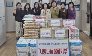 '따뜻한 가치, 섬세한 서비스, 든든한 도시관리공단 사랑나눔 물품기부 여수시도시관리공단 임직원 일동' 이라는 문구가 적힌 팻말이 세워져 있고, 그 뒤로는 '사랑나눔 물품기부' 라는 스티커가 붙은 쌀, 라면, 휴지, 생필품 박스 등이 정돈된 상태로 쌓여 있다. 해당 물품들을 기부한 여수시도시관리공단 이사장 및 임직원 9명이 물품 뒤에 서서 손가락 하트 포즈를 취하며 기념 촬영한 단체 사진이다.