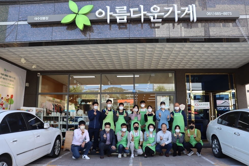 여수쌍봉점 아름다운가게 앞에서 초록색 앞치마를 입은 김유화이사장과 관계자들이 기념촬영을 하는 모습
