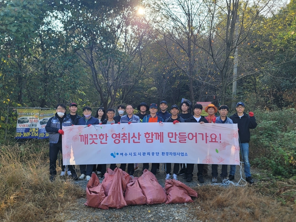 깨끗한 영취산 함께 만들어가요! / 여수도시관리공단 환경자원 사업소가 적힌 현수막을 든 사람들이 산을 배경으로 서있는 모습