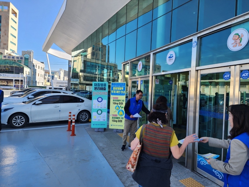 파란색 옷을 입은 사람이 건물 안으로 들어가는 사람들에게 전단지를 나눠주고 있는 모습