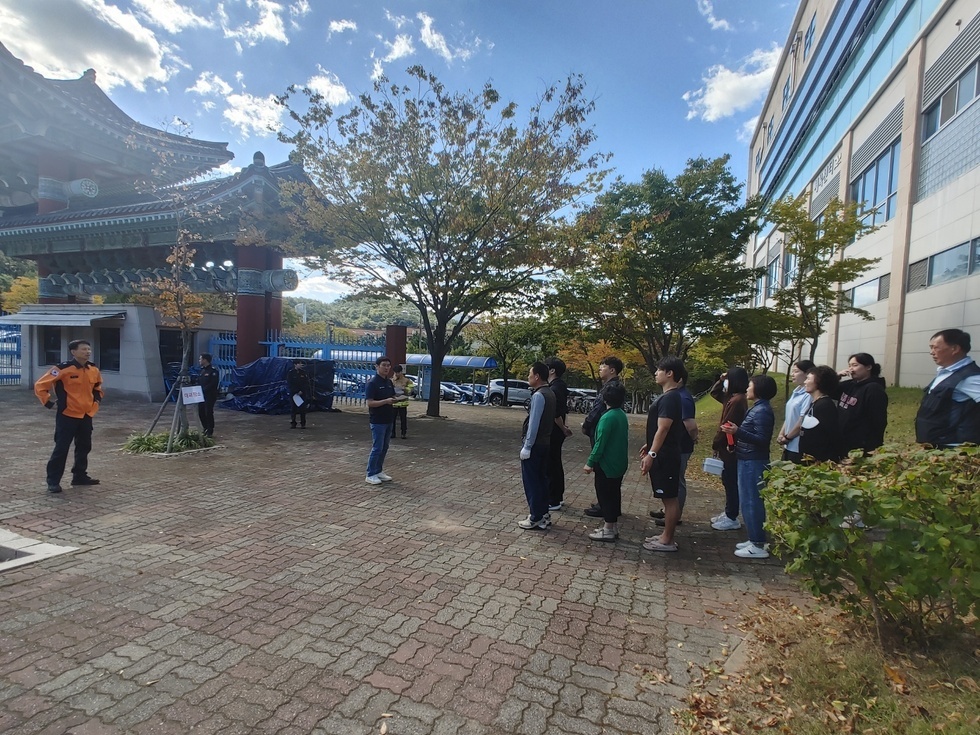 한 명의 소방 대원이 서있고 2열로 선 공단 관계자들이 설명을 듣고 있는 모습