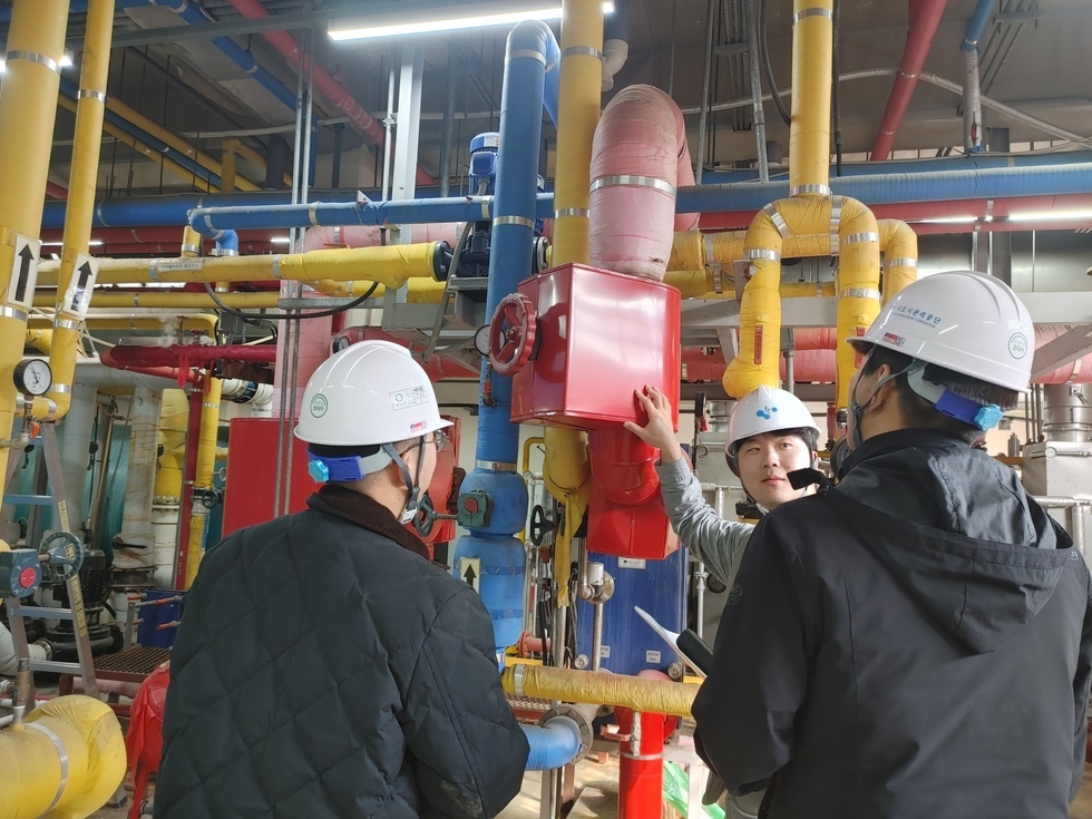 안전모를 쓴 공단 관계자들이 노란색, 빨간색, 파란색 배관이 있는 기계실에서 점검을 하고 있는 모습