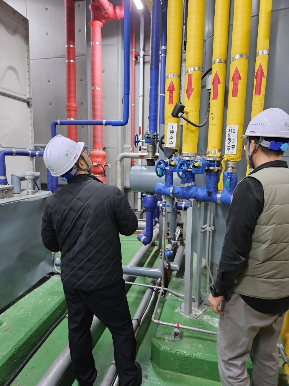 안전모를 쓴 공단 관계자들이 노란색, 빨간색, 파란색 배관이 있는 기계실에서 점검을 하고 있는 모습