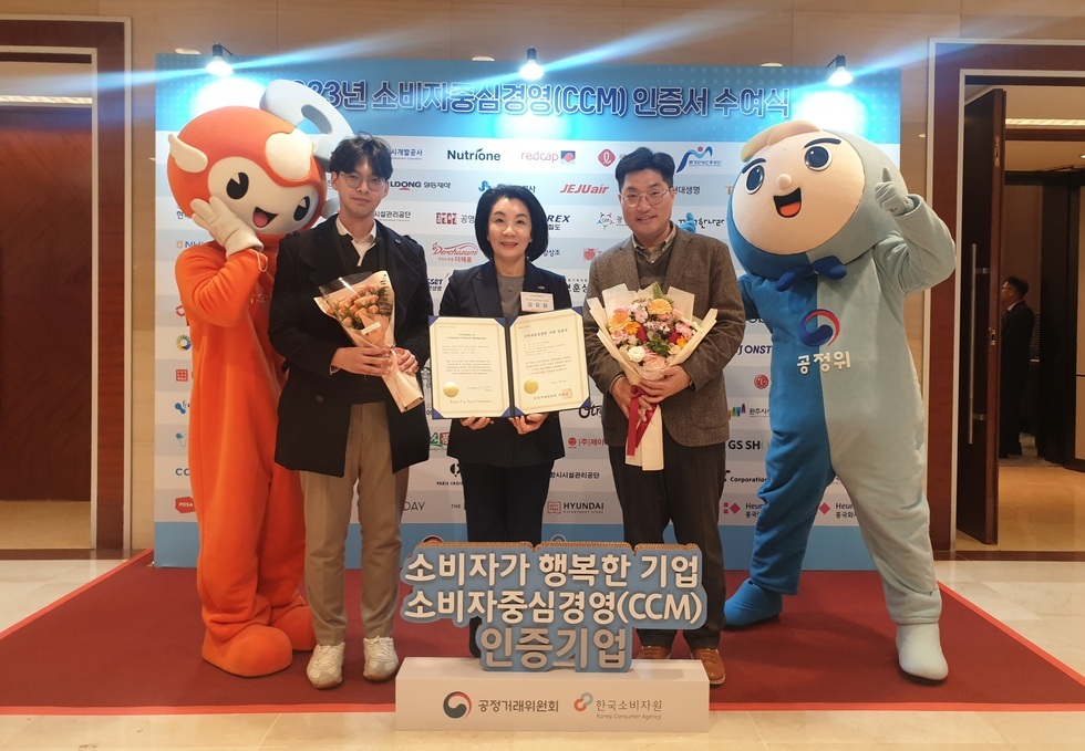 2023년 소비자 중심경영(CCM) 인증서 수여식 배경 앞에 2명의 인형탈을 쓴 사람과 3명의 사람들이 상장과 꽃다발을 들고 있는 모습