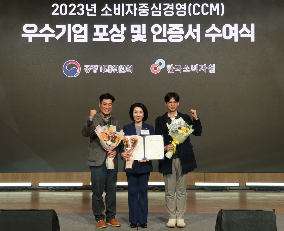 2023년 소비자 중심경영(CCM) 인증서 수여식 배경 앞에 3명의 사람들이 상장과 꽃다발을 들고 있는 모습