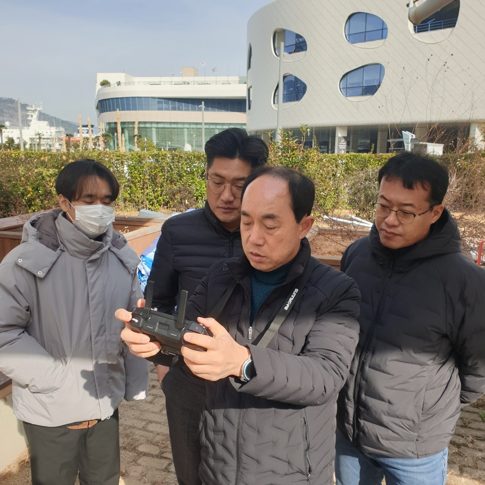 한명의 남성이 드론 리모컨을 들고 뒤에 3명의 남성들이 보고 있는 모습