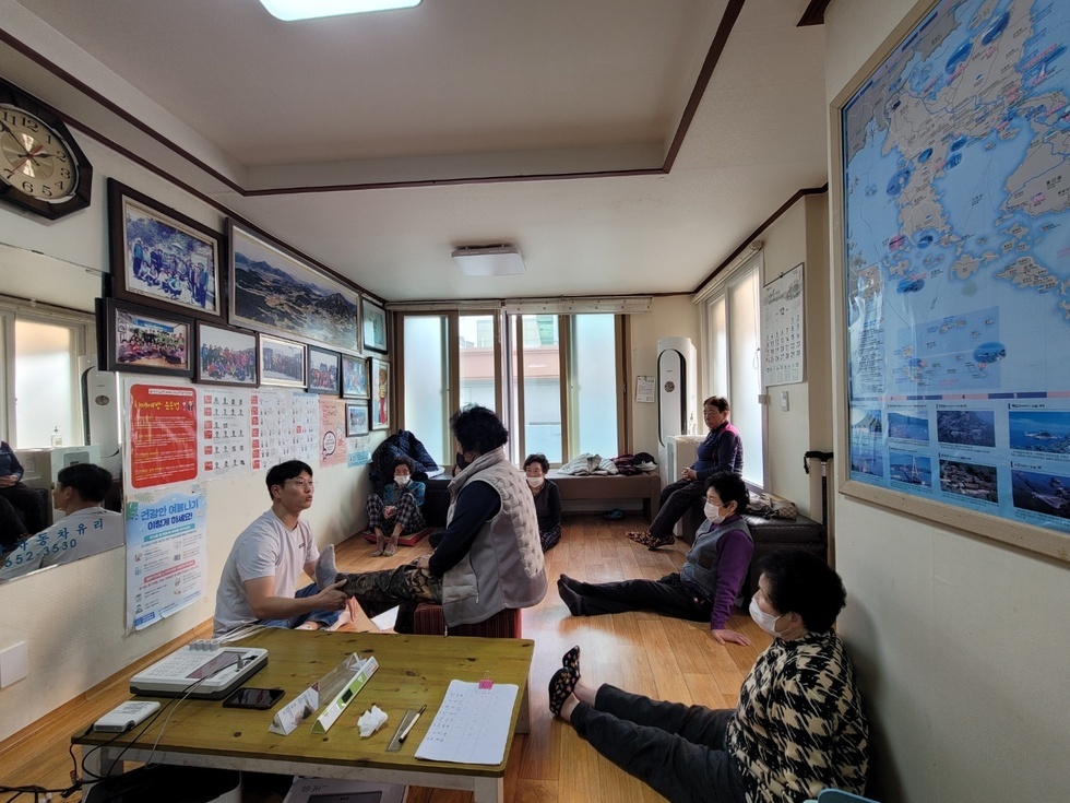 노인들은 앉아 있고,  봉사자들이 봉사활동을 하고 있는 경로당 내부의 모습