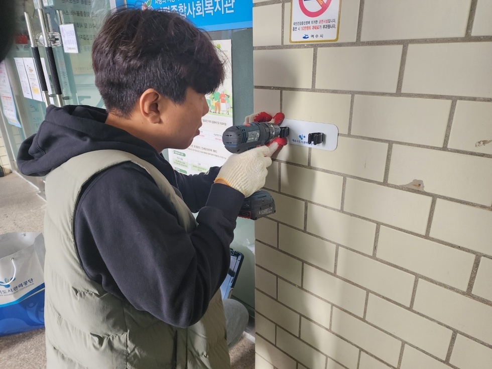 한 명의 남성이 전동 드릴을 사용하여 벽에 고정 장치를 설치하고 있는 모습