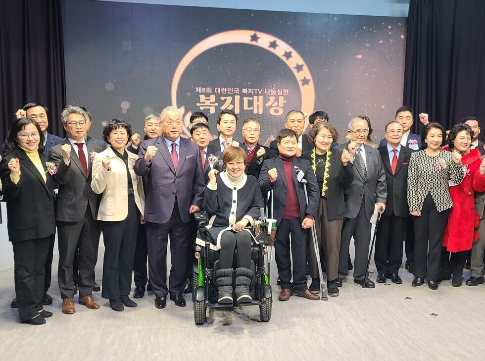 휠체어를 탄 여성 뒤로 관계자들이 서서 사진을 찍고 있는 모습