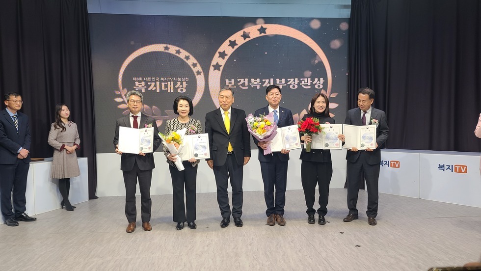 6명의 사람들이 상장과 꽃다발을 들고 서서 사진을 찍고 있는 모습