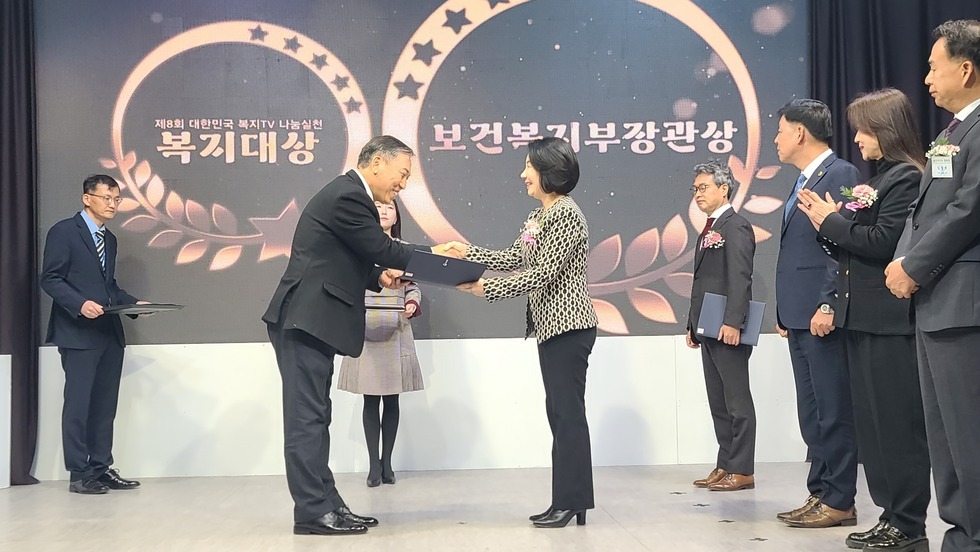 2명의 사람이 상장과 악수를 나누고 오른쪽에 4명의 사람들이 서 있는 모습