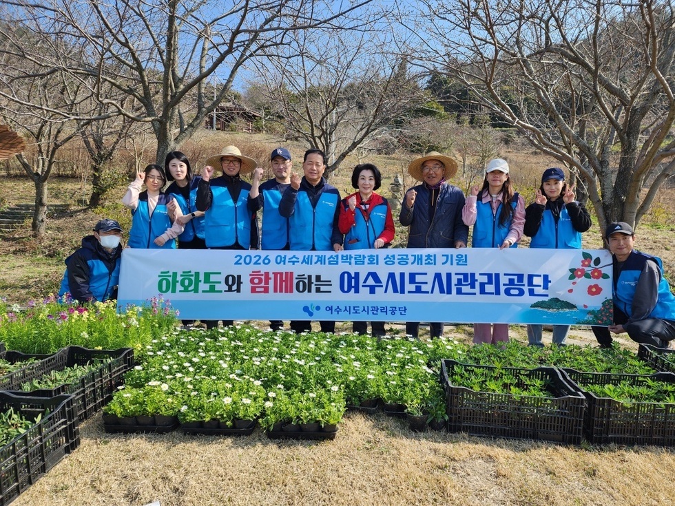 하화도에서 꽃 모종심기 업무지원에 나선 여수도시관리공단 임직원들이 현수막(2026여수세계섬박람회 성공개최 기원 하화도와 함께하는 여수시도시관리공단)을 펴고 모두 함께 단체 기념 촬영을 하고 있는 모습