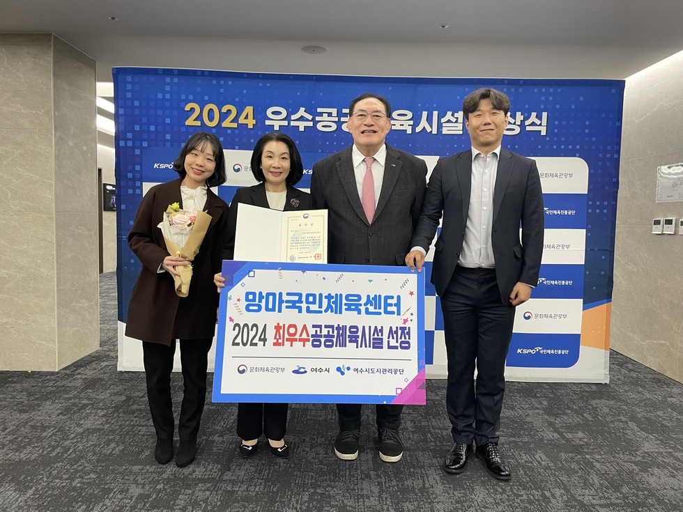 '2024 우수공공체육시설 시상식' 문구가 적힌 현수막 앞에서
4명의 사람들(왼쪽부터 꽃다발을 들고있는 젊은여성, 상장을 들고있는 중년여성, 중년남성, 젊은남성)이  
'망마국민체육센터
2024 최우수공공체육시설 선정
문화체육관광부 여수시 여수시도시관리공단' 문구가 적힌 팜플렛을 들고 있는 모습을 찍은 사진이다.