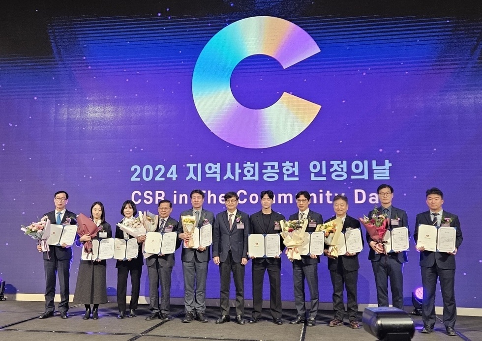 '2024년 지역사회공헌 인정의날 CSR in The Community Day' 문구가 띄워진 스크린 앞에서 10명의 수상자들이 주관사 관계자와 함께 상장과 꽃다발을 들고 기념 촬영을 하는 모습