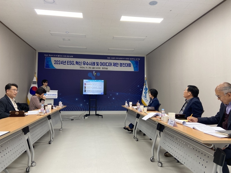 '미션: 여수시 도시발전과 시민 공감 실현
버전: 사회적 가치 실현으로 시민과 상생하는 공기업
2024년 ESG.혁신 우수사례 및 아이디어 제안 경진대회
2024. 11. 29. (금) 14:00 회의실' 문구가 적힌 현수막이 걸려있는 벽 앞에서 한 젊은 남성이 발표를 하고 5명의 임직원(중년남성 3명, 중년여성 2명)이 책상에 앉아서 심사를 하고 있는 모습이다.