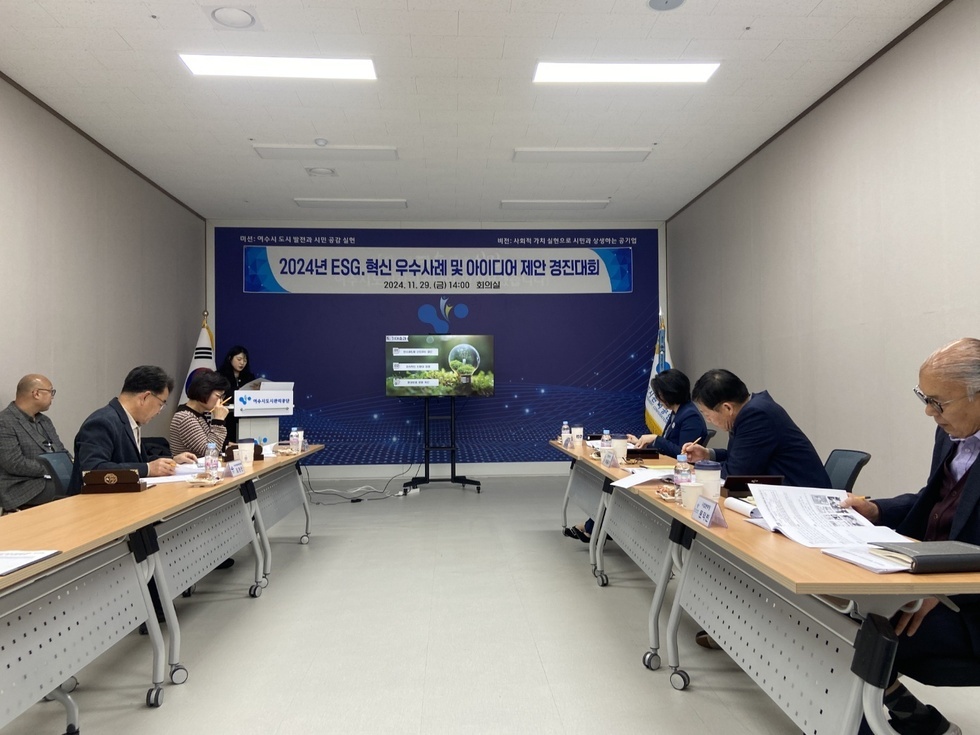 '미션: 여수시 도시발전과 시민 공감 실현
버전: 사회적 가치 실현으로 시민과 상생하는 공기업
2024년 ESG.혁신 우수사례 및 아이디어 제안 경진대회
2024. 11. 29. (금) 14:00 회의실' 현수막이 걸려있는 벽 앞에서 한 젊은 여성이 발표를 하고 5명의 임직원(중년남성 3명, 중년여성 2명)이 책상에 앉아서 심사를 하고 있고, 한 중년 남성이 의자에 앉아서 대기하는 모습이다.