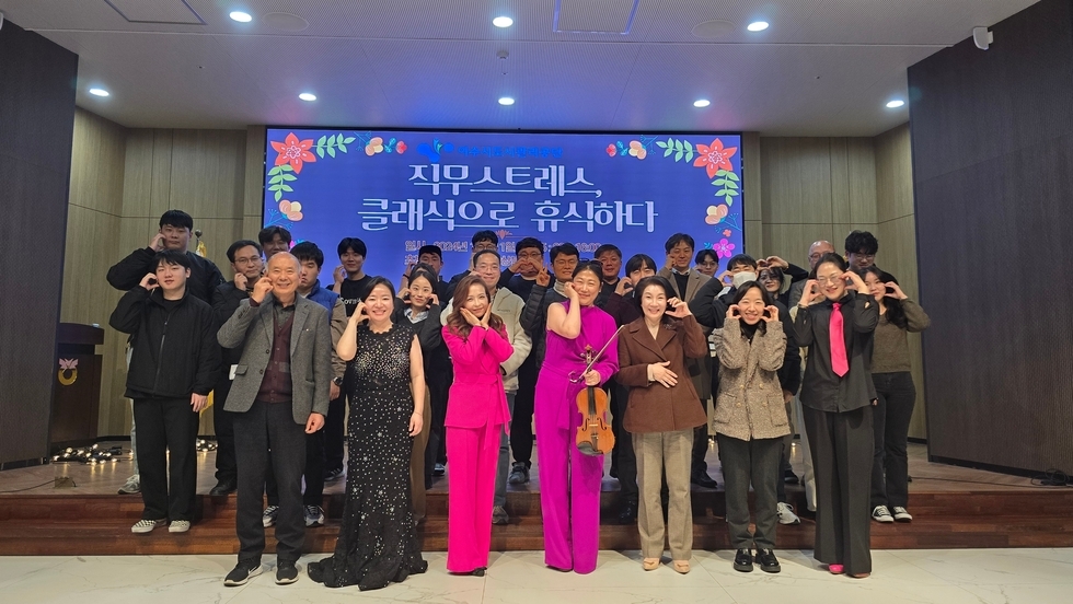 '직무스트레스 클래식으로 휴식하다' 문구가 적힌 스크린 앞에서 여러 명의 직원들을 비롯한 연주자들이 손을 볼에다 붙여서 하트를 만들고 찍은 사진이다.