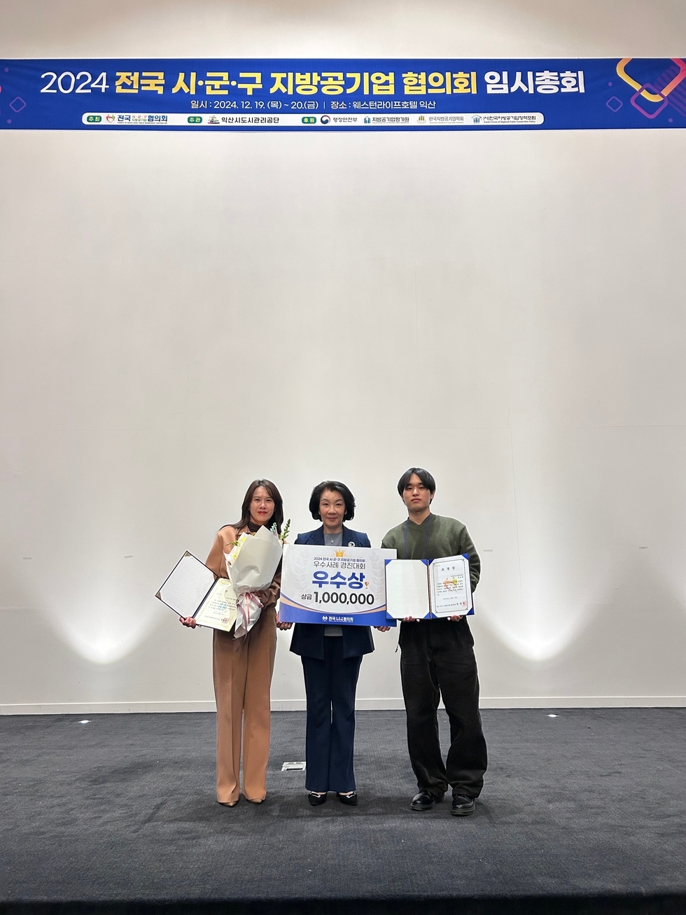 2024 전국 시,군,그 지방공기업 협의회 임시총회 일시:2024.12.19.(목)~20.(금) | 장소:웨스턴라이프호텔 익산 주최 전국시군구협의회 주관 익산도시관리공단 후원 행정안전부 지방공기업평가원 한국지방공기업학회 지방공기업정책포럼 우수사례 경진대회 우수상 상금 1,000,000이라고 적힌 팜플렛과 상장 및 표창장을 들고 사진을 찍고 있는 이사장과 직원들