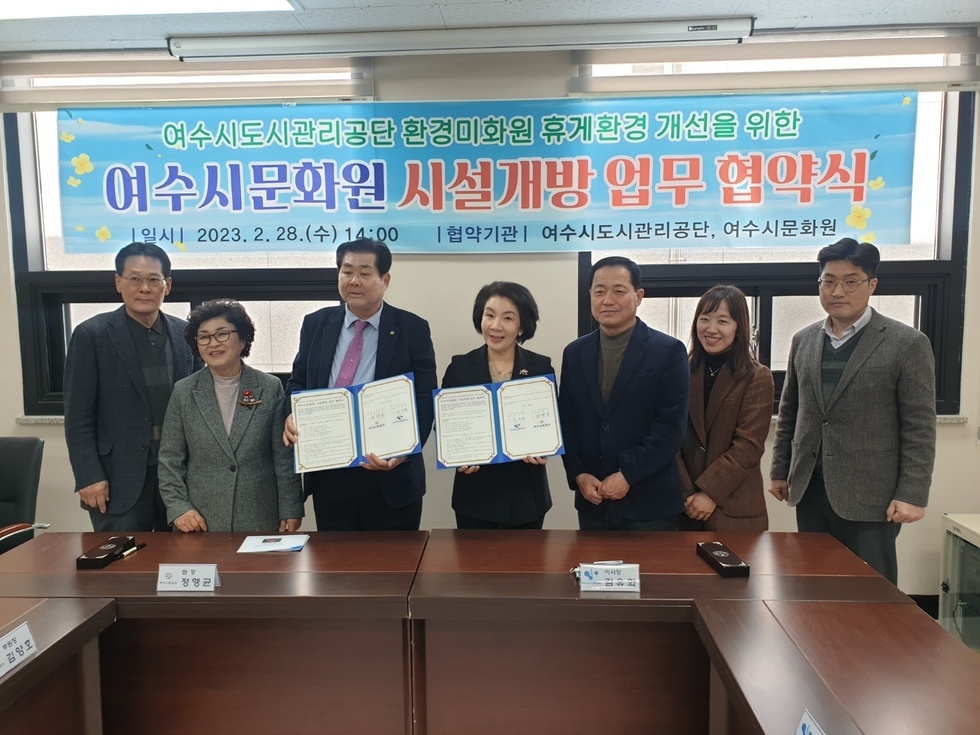  ‘여수시도시관리공단 환경미화원 휴게환경 개선을 위한 여수시문화원 시설개방 업무 협약식 |일시| 2023. 2. 28 (수) 14:00 |협약기관| 여수시도시관리공단, 여수시문화원’ 현수막을 배경으로 7명의 여수시도시관리공단과 여수시문화원 관계자들이 협약서를 들고 단체 기념사진을 촬영하고 있다. 중앙에 위치한 50대 남 녀 두 명의 인물이 협약서를 펼쳐 보이고 있으며, 양측 관계자들이 나란히 서서 밝은 표정으로 카메라를 응시하고 있다. 협약식은 실내 회의실에서 진행되었다.