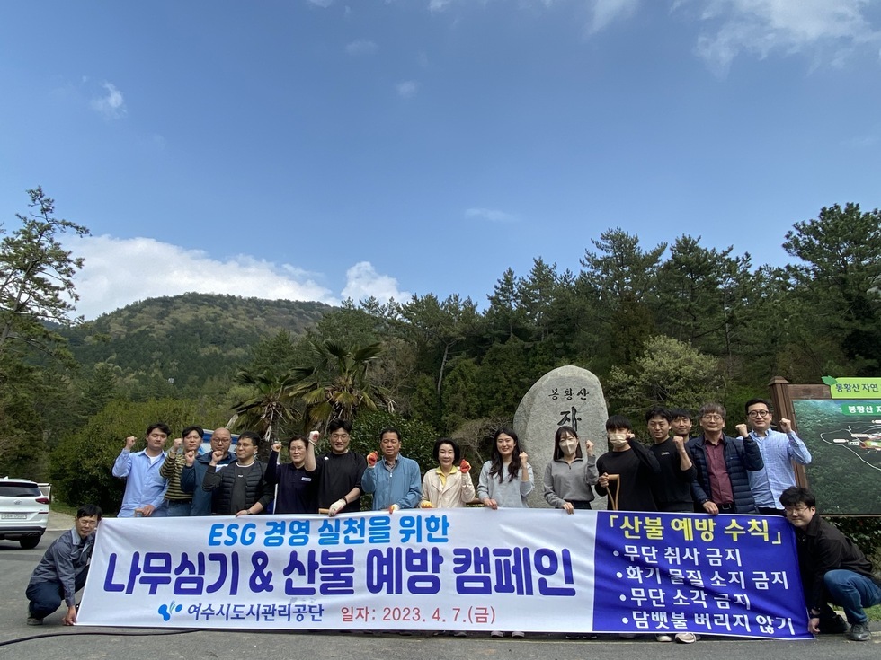 'ESG 경영 실천을 위한 나무심기 & 산불 예방 캠페인 여수시도시관리공단 일자 : 2023. 4. 7. (금) '이라는 문구가 적힌 현수막을 들고 20여 명의 여수시도시관리공단 직원들이 봉황산 입구에서 기념촬영을 하고 있다. 참가자들은 각자 장갑을 끼고 주먹을 쥐거나 손을 흔들며 캠페인 참여 의지를 나타내고 있다. 배경에는 산과 푸른 하늘, '봉황산'이라고 새겨진 바위가 함께 보이며 자연 친화적인 분위기를 더한다. 연령대는 20대부터 60대까지 다양하다.