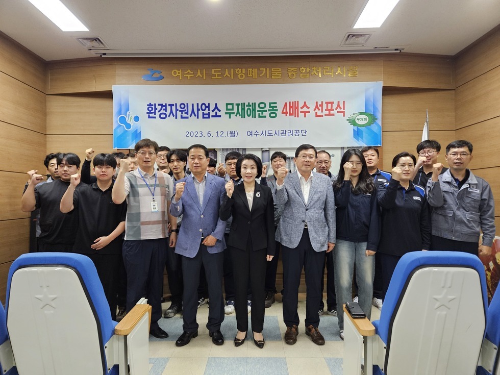 '환경자원사업소 무재해운동 4배수 선포식 2023. 6. 12 (월) 여수시도시관리공단' 현수막이 걸린 배경으로 임직원들이 단체 기념촬영을 하고 있다. 약 20명의 직원들이 모두 손을 들고 의지를 다지며 포즈를 취하고 있다.