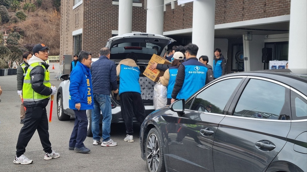 파란색 조끼를 입고 있는 「동행」봉사단이 모두 힘을 모아 차에 '나눔 보따리'를 차에 실어 놓고 있는 사진