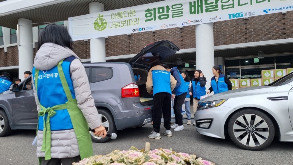 여수시도시관리공단 파란색 조끼를 입고 있는 남자 두 명이 '아름다운 나눔 보따리'를 차에 실어 놓고 있는 모습