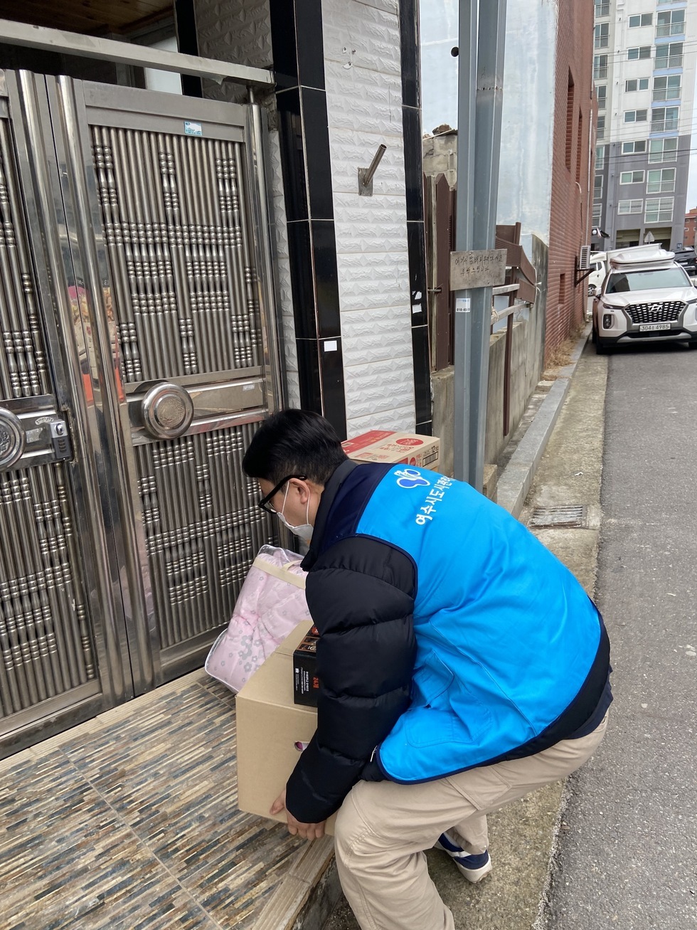 여수시도시관리공단 파란색 조끼를 입고 있는 남자 한 명이 '아름다운 나눔 보따리'를 문 앞에 놓고 있는 사진