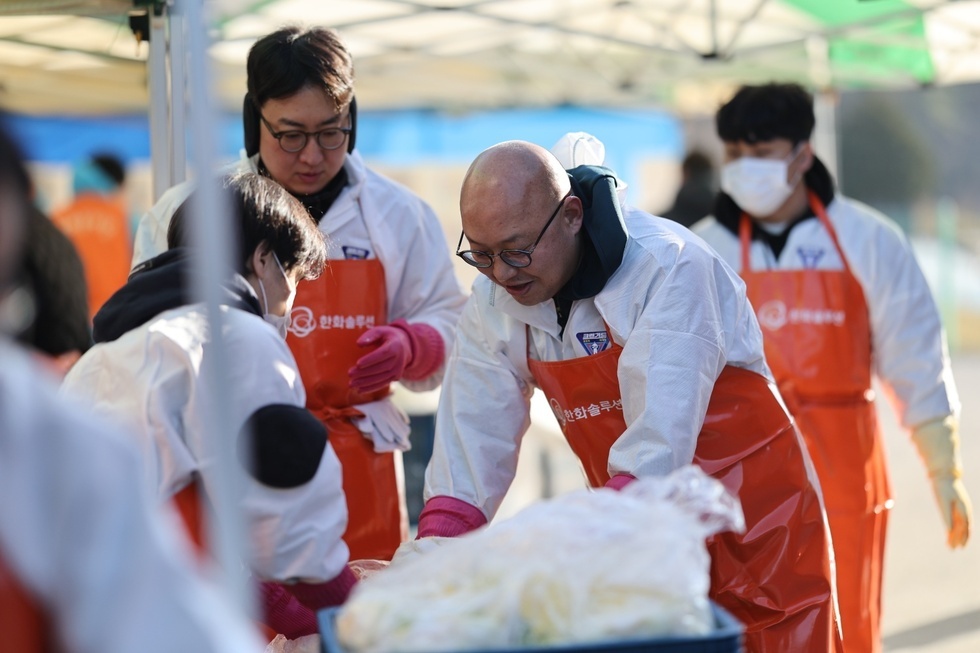 김장 나눔 봉사 현장에서 여수시도시관리공단 4명의 남성 임직원들이 하얀 방역복과 주황색 앞치마, 고무장갑을 착용한 채 배추를 다듬고 있는 모습이다. 