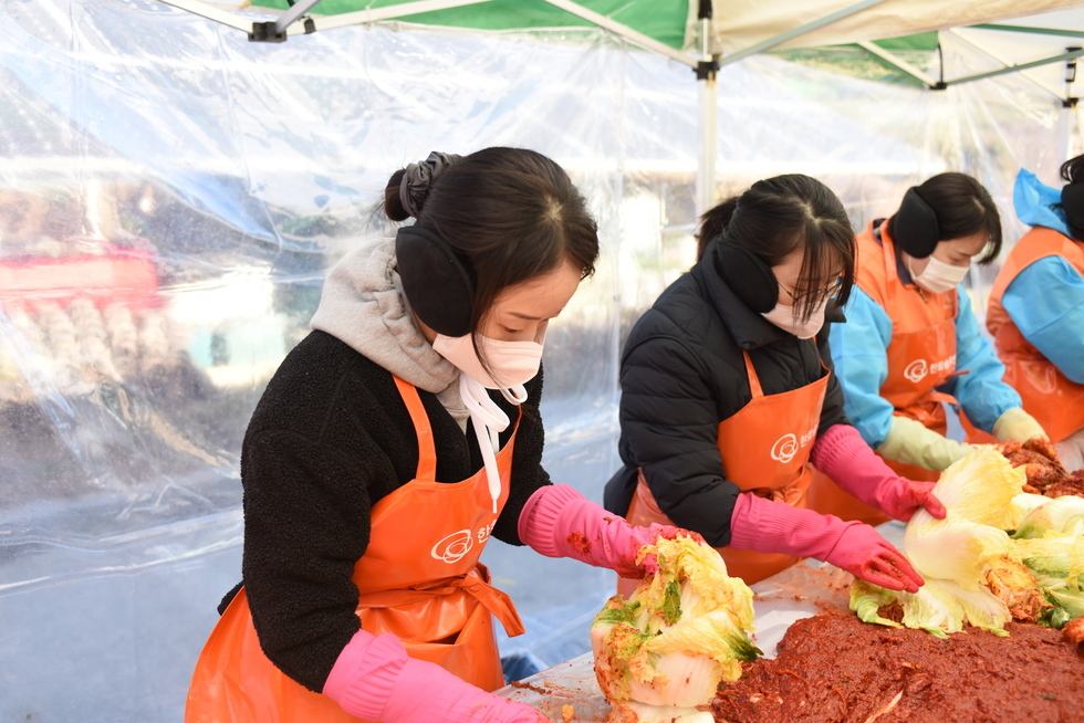 주황색 앞치마를 입고 마스크를 낀 3명의 여자 참가자들이 김장을 하고 있는 모습이다. 
