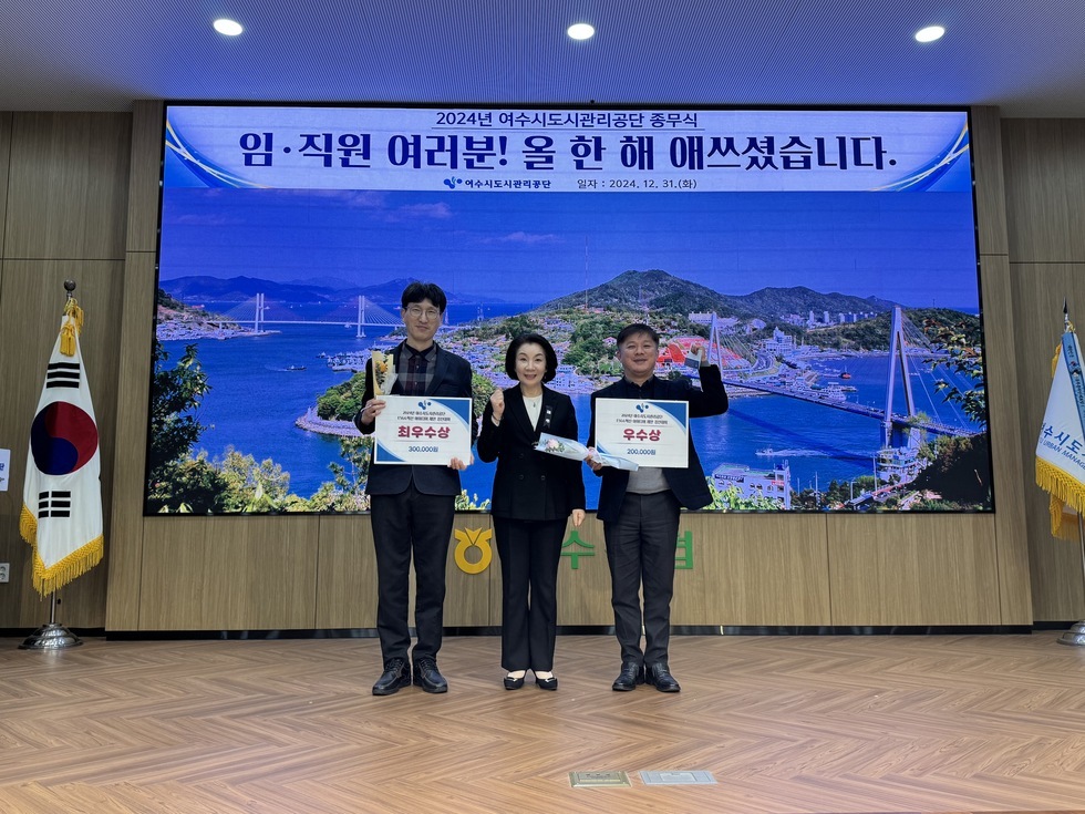 '2024년 여수시도시관리공단 종무식 임·직원 여러분! 올 한 해 애쓰셨습니다. 여수시도시관리공단 일자 : 2024.21.31 (화)'라는 문구가 적힌 대형 화면을 배경으로  3명의 임직원들이 포즈를 취하며 사진을 찍고 있다. '최우수상' , '우수상' 상장과 함께 꽃다발을 들고 있으며, 함께 기념 촬영한 임직원들은 30대부터 50대까지의 연령대로 구성되어 있다. 