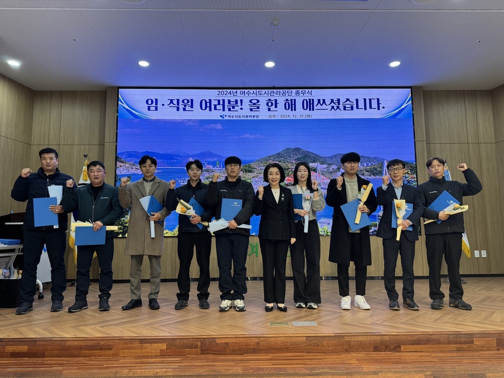 '2024년 여수시도시관리공단 종무식 임·직원 여러분! 올 한 해 애쓰셨습니다. 여수시도시관리공단 일자 : 2024.21.31 (화)'라는 문구가 적힌 대형 화면을 배경으로  10명의 임직원들이 포즈를 취하며 사진을 찍고 있다. 상장과 함께 꽃다발을 들고 있으며, 함께 기념 촬영한 임직원들은 30대부터 50대까지의 연령대로 구성되어 있다. 