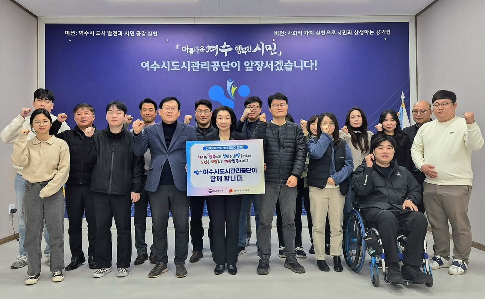 '미션 : 여수시 도시 발전과 시민 공감 실현 비전 : 사회적 가치 실현으로 시민과 상생하는 공기업 아름다운 여수 행복한 시민 여수시도시관리공단이 앞장서겠습니다!' 라는 문구가 적힌 보라색 배경 앞에서, 여수시도시관리공단 이사장을 중심으로 여수시도시관리공단 임직원들이 화이팅 포즈를 취하면 단체기념 촬영을 하는 모습